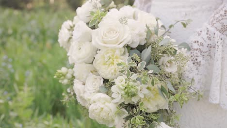 Close-Up-of-Bride-in-Her-Lace-Wedding-Gown-Holding-Bouquet-of-White-Roses-and-Greenery-in-Her-Hands-Outdoors-1080p-60fps