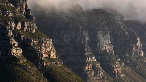 Scenic-aerial-view-of-fog-climbing-down-Twelve-Apostles-cliffs-on-Table-mountain