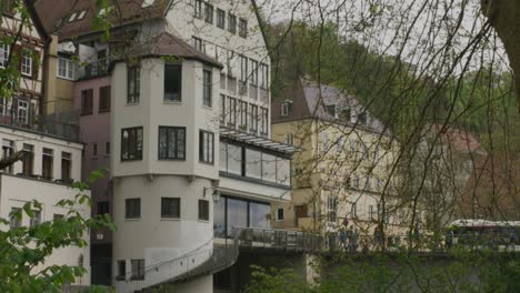 Panning-shot-from-distant-view-of-medieval-staircase-tower-to-closer-view-of-stylish-woman-on-phone-while-sitting-on-bench-in-Tubingen-downtown-river-in-Balvaria,-Germany,-Europe