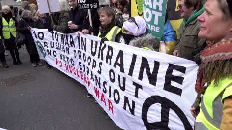 People-hold-a-white-banner-that-reads-in-black-and-red-writing,-“No-to-war-in-Ukraine,-Russian-troops-out,-no-NATO-expansion,-no-nuclear-war”-on-a-protest-opposing-the-Russian-invasion-of-Ukraine