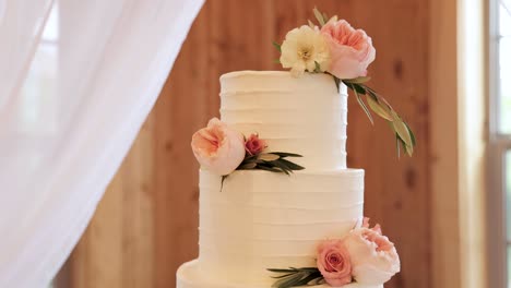 Close-Up-of-Round,-Layered-Wedding-Cake-on-a-Table-Decorated-with-White-Textured-Frosting-and-Pink-Flowers-1080p-60fps