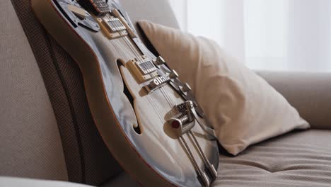 Semi-acoustic-electric-guitar-on-sofa-in-empty-living-room,-no-people,-closeup-view