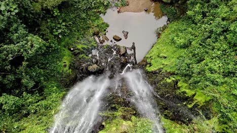 DRONE-AERIAL-SHOT-ZOOMING-IN-WATERFALL-SURROUNDED-BY-TREES