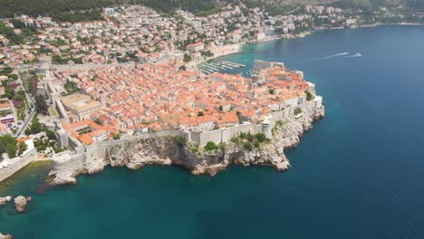Aerial-rotating-shot-of-old-town-Dubrovnik,-Croatia-with-rocky-cliffs-along-the-seaside-and-fortress-walls-visible-from-above-on-a-sunny-daytime