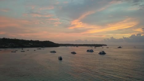 Gorgeous-aerial-view-flight-fly-backwards-drone-footage-at-golden-hour-dream-sunset-with-colourful-clouds-mirroring-at-Mushroom-Bay-Lembongan