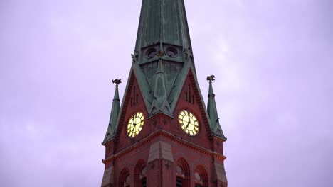 Tower-of-christian-Trinity-church-in-Arendal-Norway---Static-evening-shot-with-birds-flying-around-uplit-clock-and-sky-background