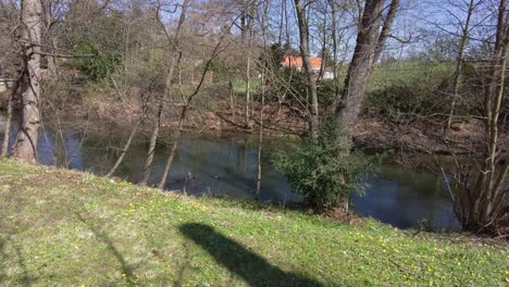 Flowing-river-in-Olomouc-park-on-a-sunny-spring-day,-shore-with-trees-and-bushes