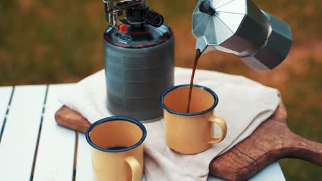 Pouring-Coffee-from-a-silver-compact-metal-kettle-into-a-yellow-rugged-mug-while-camping