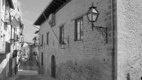 Fotografía-En-Blanco-Y-Negro-De-Edificios-Antiguos-A-Lo-Largo-De-Una-Calle-Estrecha-En-La-Antigua-Ciudad-Amurallada-De-Morella-En-Castellón,-España