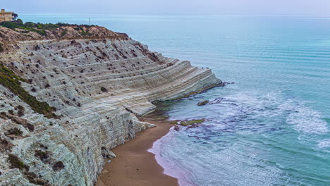 High-angle-shot-over-the-Scala-dei-Turchi,-a-rocky-cliff-on-the-southern-coast-of-Sicily,-Italy-with-waves-crashing-on-in-timelapse-at-daytime