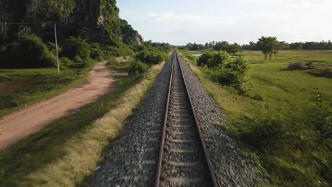 Straight-narrow-gauge-rail-way-track-travels-to-one-point-perspective-on-the-horizon,-drone-fly-over-it-the-Cambodia-countryside,-SE-Asia
