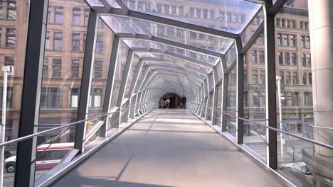 A-lone-man-walks-away-along-the-hypnotic-geometric-steel-glass-Bridge,-CF-Toronto-Eaton-Centre,-in-Ontario,-Canada-shopping-mall---bridge-above-road-with-view-of-street-below