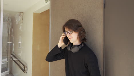 Young-man-with-glasses,-headphones-around-his-neck,-talking-on-his-mobile-phone