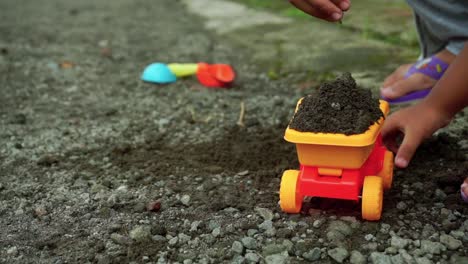 Hands-of-a-Happy-Kid-Playing-with-stone,-sand-and-truck-toys-on-the-road