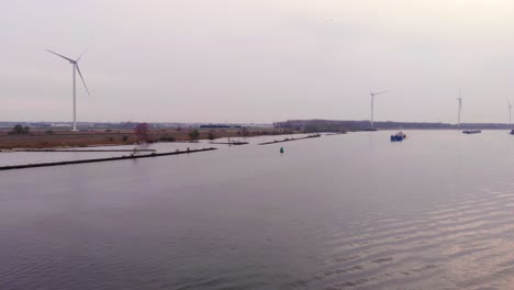 Aerial-Dolly-Forward-Over-Oude-Maas-With-Still-Wind-Turbines-And-Torpo-Cargo-Ship-Approaching-In-Distance