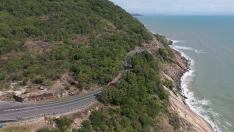 Captain-Cook-Highway-vertical-aerial-with-red-car-and-coastline,-Queensland,-Australia