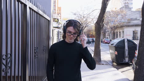 Young-man-with-glasses-and-headphones-smiles,-walking-and-listening-to-music-on-the-street