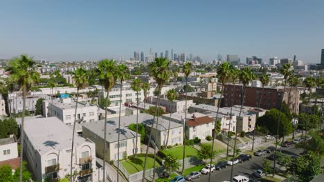 Aerial-Drone-Shot-Over-Tree-Lined-Los-Angeles-Streets,-Apartment-Rooftops-Below-and-Downtown-LA-Skyscrapers-Ahead