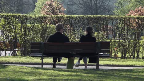 Two-people-enjoying-a-chat-whilst-sitting-on-a-bench-in-a-park-during-a-sunny-spring-day