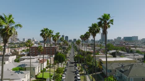 Flying-Through-Los-Angeles-Streets-on-a-Sunny-Day-in-California,-Drone-Aerial-Shot-Through-Palm-Tree-Lined-Street