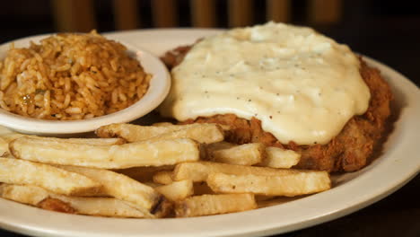 Chicken-fried-steak-smothered-in-peppered-country-gravy-with-dirty-rice-and-french-fries,-slider-close-up-4K