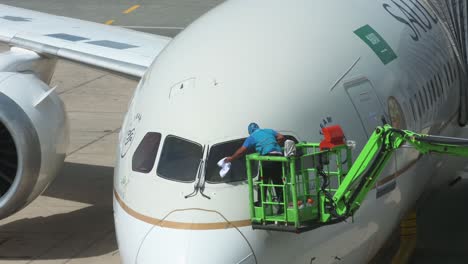 Ein-Arbeiter-Reinigt-Die-Frontscheibe-Eines-Flag-Carriers,-Saudi-Arabiens,-Einer-Saudischen-Fluggesellschaft,-Ein-Flugzeug-Ist-Auf-Der-Landebahn-Des-Internationalen-Flughafens-Jeddah-Zu-Sehen