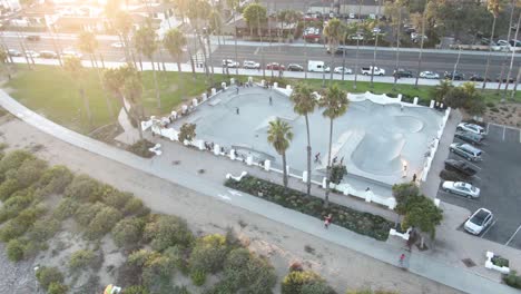 Kreisförmige-Antenne-Nummer-3-Eines-Skateboardparks-Bei-Sonnenuntergang-Mit-Jungen-Erwachsenen-In-Der-Nähe-Des-Strandes-Und-Der-Belebten-Autobahn-In-Santa-Barbara,-Kalifornien,-USA