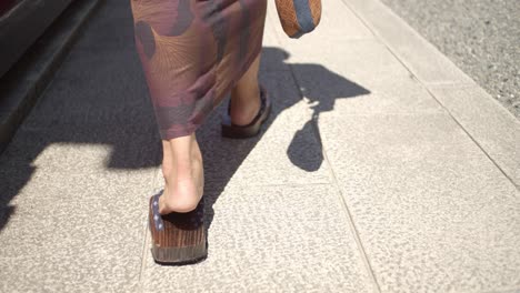 Guy-wearing-a-yukata-wearing-traditional-wooden-sandles-walking-towards-a-temple-in-Kyoto,-Japan-soft-lighting-slow-motion-4K