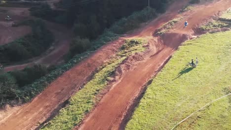 Drone-shot-of-motocross-riders-riding-motorbikes-on-dirt-park-track-over-the-left-turn-and-jump-fast