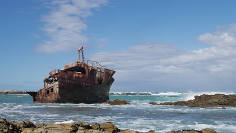 Old-weathered-shipwreck-in-shallows-with-waves-running-in,-rocky-coastline-of-L'Agulhas,-South-Africa,-static-shot