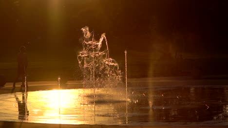 Mother-and-kid-playing-with-water-fountain-against-a-background-of-sunset