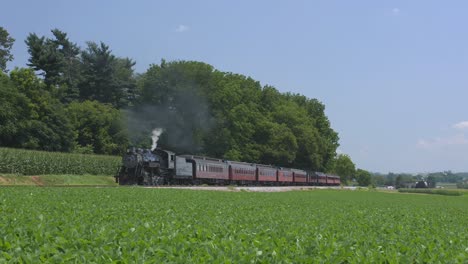 Una-Máquina-De-Vapor-De-1924-Con-Un-Tren-De-Pasajeros-Que-Echa-Humo-Y-Viaja-A-Lo-Largo-De-La-Campiña-Amish-En-Un-Día-De-Verano