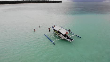 4K-aerial-orbiting-shot-of-people-waving-on-anchored-banca-pontoon-boat-in-calm-ocean-waters-of-Balabac-Palawan-in-the-Philippines