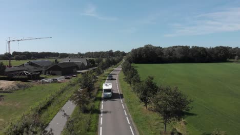 Aerial-follow-of-a-camper-on-a-clean-asphalt-country-road-in-The-Netherlands-with-a-row-of-trees-against-a-blue-sky