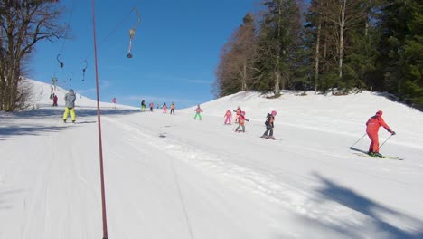 A-ski-lift-going-uphill-with-skiers-and-a-group-of-children-with-a-trainer-descending-one-after-another-down-the-hill