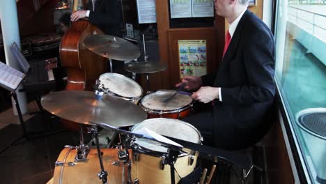 Caucasian-drummer-playing-the-drums-while-wearing-a-suit-and-tie-on-a-boat