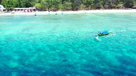 Traditional-Balinese-boat-turning-around-in-the-crystal-clear-sea-water-near-the-white-sandy-beach