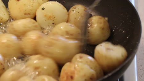 Closeup-of-small-potatoes-being-sautÃ©ed-in-a-pan-with-bubbling-butter,-garlic-and-chopped-herbs-on-a-gas-stove