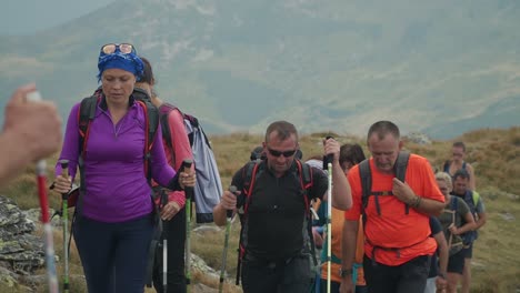 A-large-group-of-people-with-trekking-poles-hike-up-the-to-the-summit-of-Pietrosu-Rodnei,-Romania