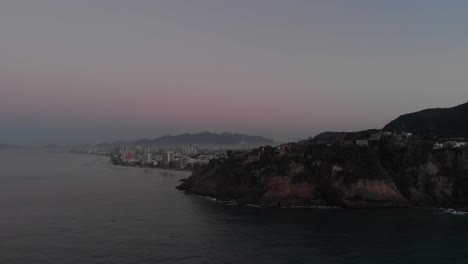 Luftschwenk,-Der-Das-Weitläufige-Viertel-Barra-Da-Tijuca-In-Rio-De-Janeiro-Mit-Morgennebel-Hinter-Den-Klippen-Des-Strandes-Von-Joatinga-Freigibt