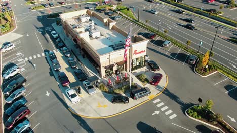 Aerial-tilt-up-reveals-Chick-fil-A-two-lane-busy-drive-through,-American-flag