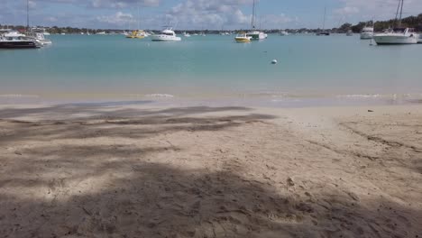 A-reveal-shot-from-the-sand-of-a-beach-to-a-panorama-view-of-a-some-anchored-boats-in-a-tropical-beach,-in-Mauritius