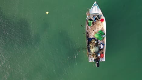 Aerial-top-down-shot-of-two-fishermen-pulling-out-net-and-fish-from-the-sea,-drone-shot