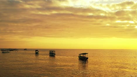 Kleine-Fischerboote-Schwimmen-Im-Ruhigen-Meer-Mit-Goldfarbenem-Horizont-Und-Spiegelung-Des-Himmels