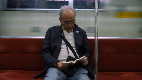 A-japanese-old-man-intently-reading-a-book-on-a-subway-train