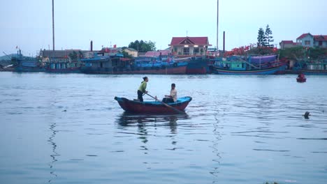Wideshot-of-Two-People-in-a-Rowboat-in-a-Small-Vietnamese-Fishing-Village