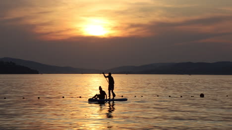 Sunset-Silhouette-Active-Couple-Stand-Up-Paddling-In-a-Tropical-Bay