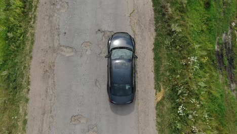 Aerial-View-of-Car-Avoiding-Potholes-On-An-Old-Road