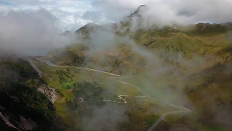 Winding-road-along-a-mountain-pass-in-the-Dolomite-Italian-Alps-with-clouds-passing-viewer,-Drone-flyover-reveal-shot