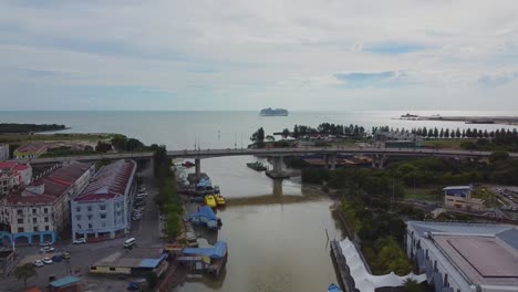 Aerial-backwards-flight-showing-cars-on-bridge-and-melaka-river-outfall-from-ocean-in-malaysia